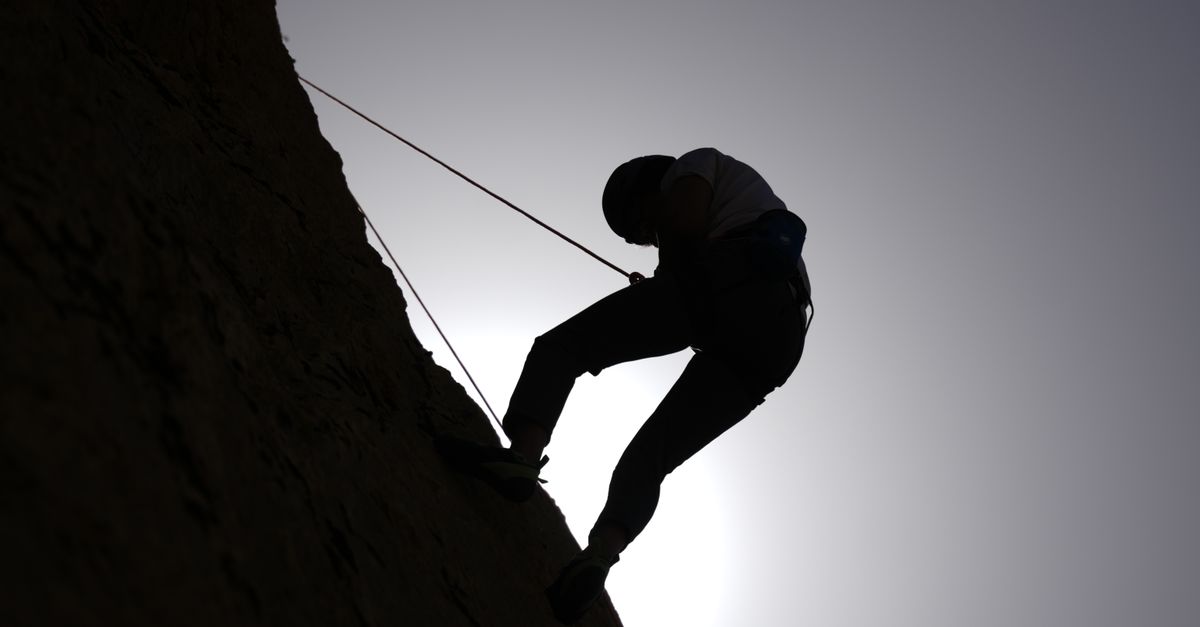 Silhouette of a person rock climbing in Damascus, Syria, against a bright sky.